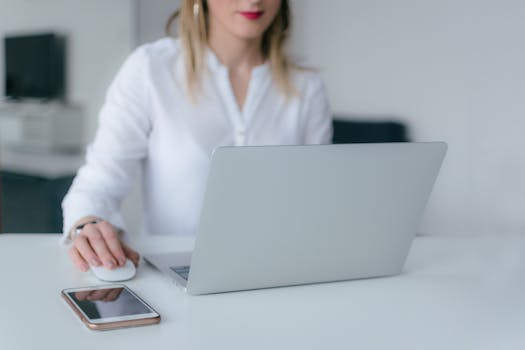 A woman working at a desk using a laptop and smartphone, exemplifying remote work.