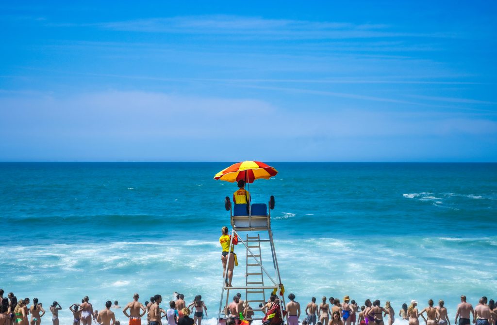 Lifeguard overlooking a crowded beach under a colorful umbrella, capturing a vivid summer day.