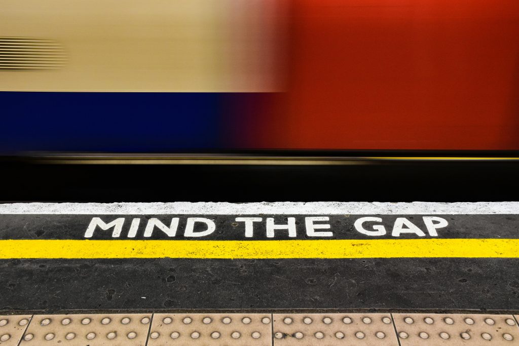 Long exposure of a train passing by a 'Mind the Gap' sign at a subway station platform.